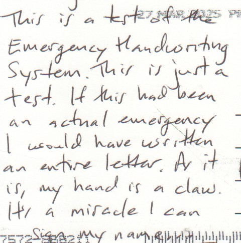 Handwritten message from a back of a postcard. The visible words read: "This is a test of the Emergency Handwriting System. This is just a test. If this had been an actual emergency I would have written an entire letter. As it is, my hand is a claw. It's a miracle I can sign my name." The letters are a mix of cursive script and block letters, all are readable, though messy.