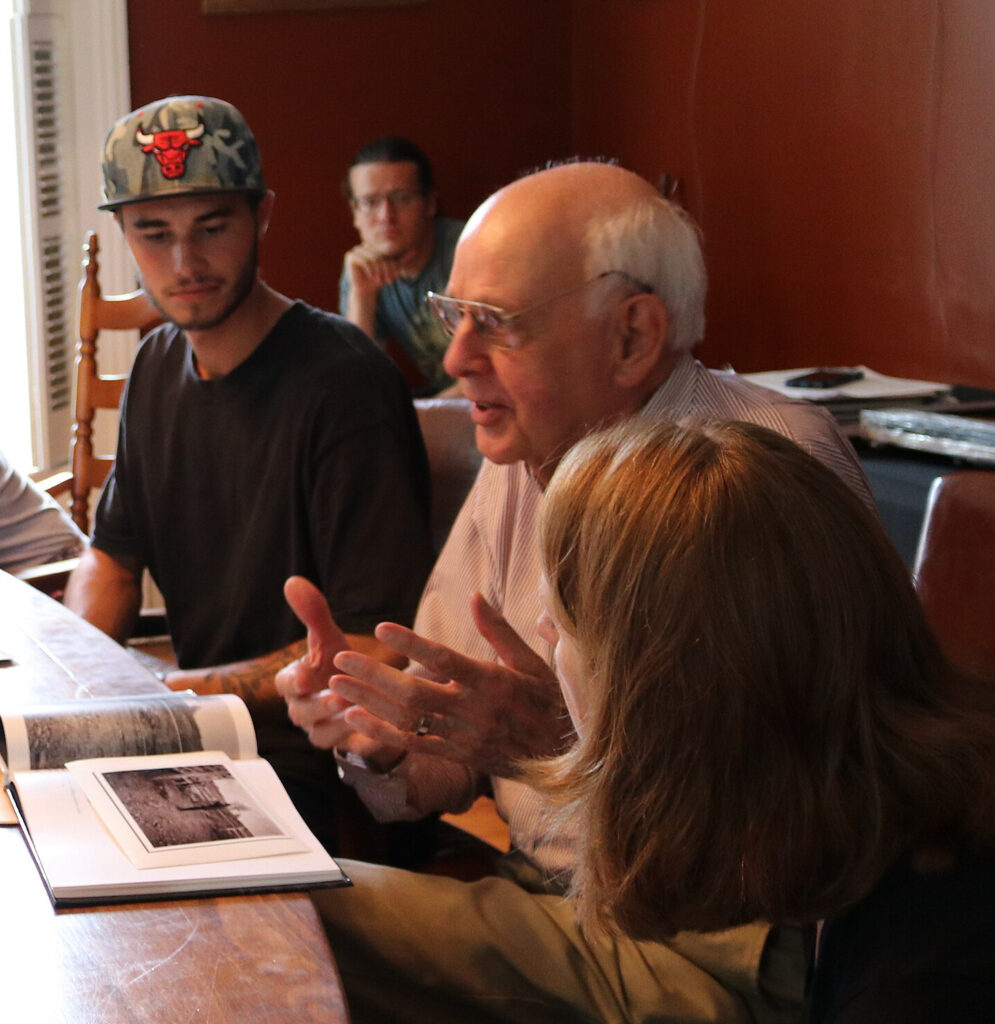 Wendell Berry sits between two students in a seminar, before him is a  book of photographs.